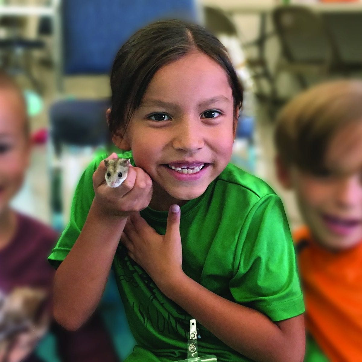 Girl with green shirt smiling and holding hamster
